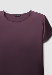 Top a maniche corte, con scollatura rotonda, di un profondo colore viola, realizzato in un tessuto liscio con una leggera lucentezza. Design pulito, senza motivi o dettagli visibili.