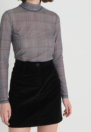 Vrouw die een nauwsluitende grijze geruite coltrui en een hooggetailleerde zwarte rok met een knoopsluiting aan de voorkant draagt.