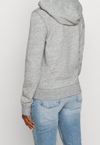 Felpa grigia con una finitura testurizzata, dotata di cappuccio e polsini a coste, abbinata a jeans azzurri chiari. Focus su un design casual e confortevole.