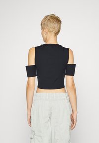 Μαύρο κοντό τοπ με ανοιχτά μανίκια, διαθέτοντας εφαρμοστή σχεδίαση και λεία υφή. Συνδυάζεται με ανοιχτό γκρι cargo παντελόνι.