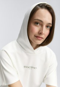 Witte hoodie met korte mouwen, een ronde zoom en kleine 'good times' tekst in het groen. Glad materiaal en een bijpassende capuchon.