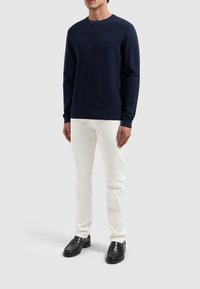 Dunkelblauer Strickpullover mit strukturiertem Muster, kombiniert mit weißen Hosen und schwarzen Loafers, mit rundem Ausschnitt und langen Ärmeln.