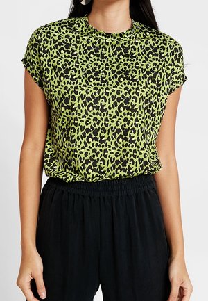 Kvinde iført en limegrøn og sort leopardprint kortærmet top, der er stoppet ned i løse sorte bukser med elastisk talje.