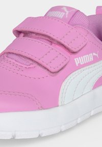 Κοντινή λήψη σε ροζ αθλητικό παπούτσι Puma με δύο λουράκια βέλκρο, λευκό λογότυπο Puma και λευκή σόλα.