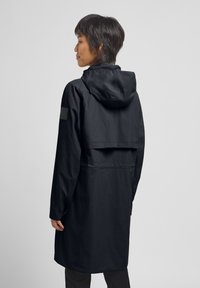 Wasserabweisende schwarze Jacke mit Kapuze, leichtes Material und lockere Passform. Sie verfügt über eine verstellbare Taille und eine Lüftungsöffnung im oberen Rückenbereich für Atmungsaktivität.