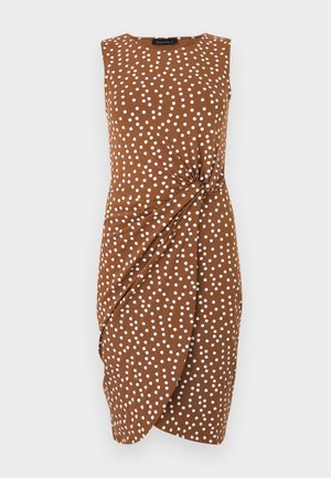 Robe marron sans manches longueur genou avec des pois blancs et un détail noué sur le côté sur un fond uni.