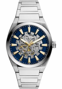 Edelstahl-Uhr mit blauem Zifferblatt, goldenen Indizes und Skelettdesign. Verfügt über ein silbernes Armband und eine Krone auf der rechten Seite.