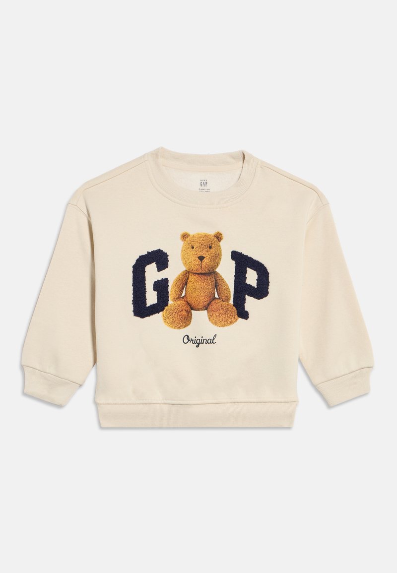 Krēmkrāsas toddler džemperis ar rotaļu lāča attēlu starp lieliem, strukturētiem tumši ziliem burtiem "G" un "P" un zem tā vārdu "Original".