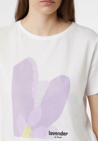 Biała bawełniana koszulka z lawendowym wzorem florystycznym w jasnym fioletowym kolorze z żółtymi akcentami oraz napisem "lavender la fleur" w czerni.
