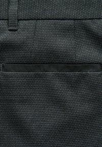 Grauer, strukturierter Stoff mit einem subtilen Muster, das über eine elegante schwarze Tasche verfügt, die in das Design integriert ist. Enger Gewebte und glatte Oberfläche.