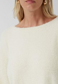 Crème-kleurige, zacht aanvoelende trui met een brede, ondiepe halslijn. Heeft een fluffy afwerking en een minimaal design, dat de nadruk legt op comfort.