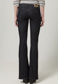 Ciemnoniebieskie dzwony z średnim stanem i jasnobrązową skórzaną metką z tyłu. Posiadają dwie tylne kieszenie oraz kontrastowe rękawy.