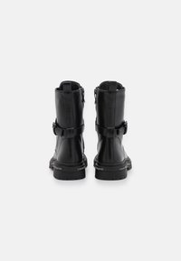 Botines de cuero negro con punta redondeada, cremalleras laterales dobles y correas decorativas. Suelas de goma gruesas con detalles de marca.