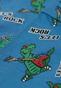 Modrá tkanina s kreslenými dinosaury, kteří nosí sluneční brýle, hrají na kytary a mají v tučném černém písmu nápis "Pojďme rockovat".