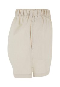 Short beige à taille élastique avec poche latérale et ourlet cousu, vu de côté sur fond blanc.