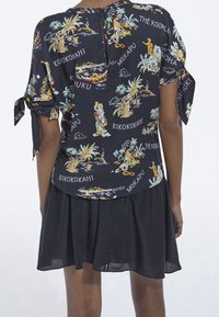 Blusa nera a maniche corte con stampa tropicale colorata, che include palme e figure, con schiena a chiave e maniche legate.