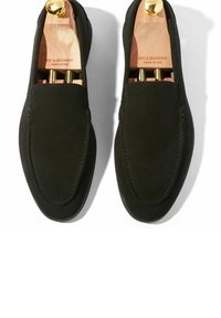 Zwarte suède instappers met een afgeronde neus, licht verhoogde stiksels en houten schoenenzorgers binnenin. Gouden hardware-accenten op de hak.