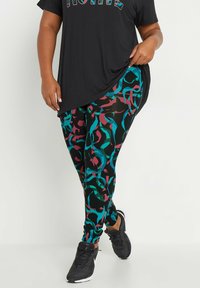 Mustat legginsit, joissa on monivärinen abstrakti kuvio turkoosin, burgundin ja mustan sävyissä. Yhdistetty löysään mustaan puseroon ja mustiin lenkkareihin.