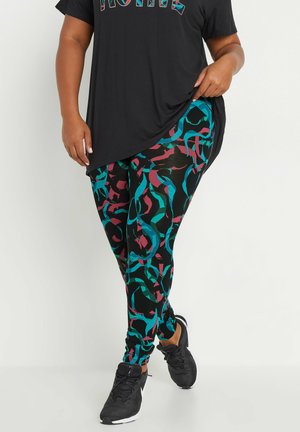 Zwarte leggings met een multikleurig abstract patroon in teal, bordeauxrood en zwart. Gepaard met een losse zwarte top en zwarte sneakers.