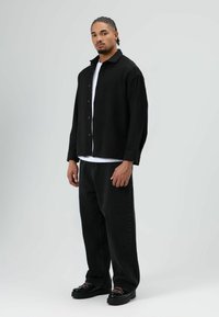 Zwart overhemd over een wit T-shirt, gecombineerd met zwarte baggy jeans en zwarte platform schoenen met contrasterende roze veters.