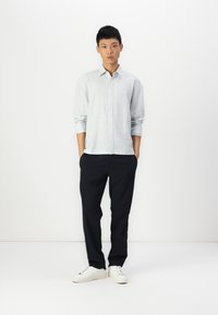 Camisa listrada azul-claro com design de botões, combinada com calças escuras azul-marinho. Modelo usa ténis brancos. Tecido suave, corte descontraído.