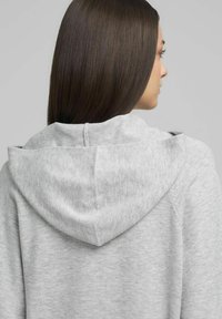 Sudadera gris con capucha y textura suave, que presenta una capucha prominente, mangas raglán y un diseño sencillo y minimalista.
