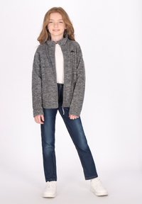 Giacca grigia con zip e colletto alto, abbinata a jeans blu e sneakers bianche. Tessuto morbido con un design minimalista.