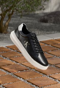 Zwarte leren sneaker met witte accenten, vetersluiting en een gestructureerde loopzool. Beschikt over een logodetail op de zijkant.