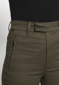Olivgröna byxor i strukturerad tyg, med en dragkedjeficka och sydda detaljer, platt midjeband och bälteshällor.