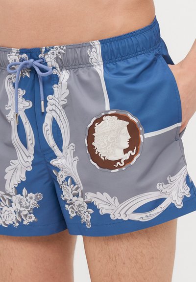 Shorts de bain bleus et gris avec motifs floraux, taille élastique, cordon de serrage, et un médaillon avec un visage en relief.