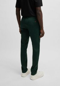 Zielone bawełniane spodnie o dopasowanym kroju, z tylną kieszenią i gładką teksturą. W połączeniu z białymi trampkami.