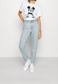 Bílý tričko s černým grafickým potiskem Mickey Mouse, spárované se světle modrými džínami s vysokým pasem a bílými teniskami. Jednoduchý, pohodlný střih.