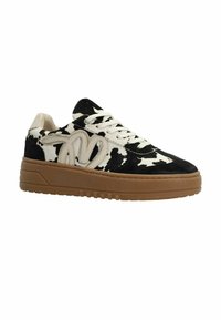 Sneaker en imprimé vache noir et blanc avec texture en daim, accents crème, lacets blancs et semelle en caoutchouc marron épaisse. Dispose d'un bout arrondi et d'un col rembourré.