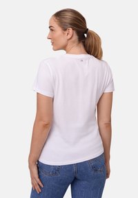 T-shirt bianca in cotone con maniche corte, scollo rotondo e piccolo logo sul retro. Abbinata a jeans in denim blu.
