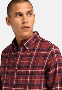 Camicia in flanella a quadri rossi e blu con colletto button-down, cuciture bianche in contrasto e un piccolo logo ricamato sul lato sinistro del petto.