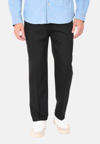 Pantaloni formali neri con design a gamba dritta, caratterizzati da una texture liscia e pieghe sottili, abbinati a sneaker bianche e una camicia azzurro chiaro.