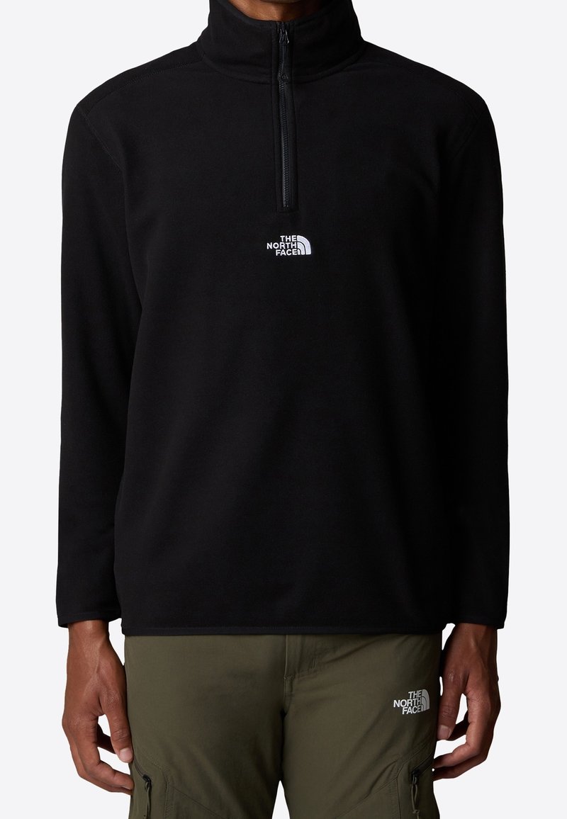 Schwarzer Fleece-Pullover mit halbhohem Reißverschlusskragen, versehen mit dem weißen North Face-Logo auf der Brust. Weiche Textur und lockere Passform.