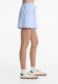 Shorts rayés bleus et blancs avec une taille élastique et une poche latérale. Associés à des baskets blanches et des chaussettes blanches côtelées.
