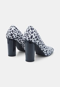 Čevlji na visoki peti z leopardjim vzorcem, z zgornjim delom iz teksturirane tkanine in sijočimi črnimi blok petami. Imajo obliko s koničastim nosom.