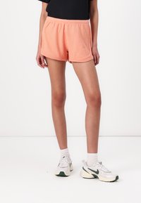 Peach ribbed shorts with an elastic waistband, featuring a loose fit and contrasting stitch detail. Paired with light-colored athletic shoes.