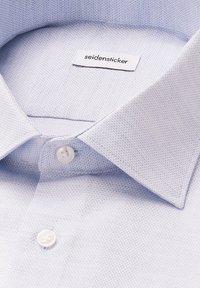 Camicia azzurro chiaro con bottoni, realizzata in tessuto testurizzato, colletto classico e bottoni bianchi singoli, con etichetta del marchio visibile all'interno.