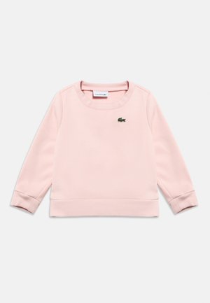 Hele roosakas pikkade varrukatega crewneck-pusafliis, millel on soonikkoes varrukapaelad ja alumine serv ning väike roheline krokodilli logo vasakul rinnal.