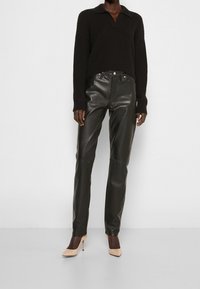 Suéter negro de punto acanalado con cuello, combinado con pantalones de cuero negro de tiro alto y tacones nude de punta, presentando una silueta elegante.