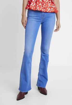 Jeans a campana blu in denim, con vita media e cuciture in contrasto, abbinati a tacchi a punta color bordeaux.