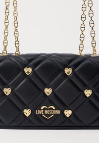 Borsa a tracolla in ecopelle trapuntata nera con dettagli a forma di cuore dorati e una catena dorata. Al centro è presente il logo "LOVE MOSCHINO" in oro.