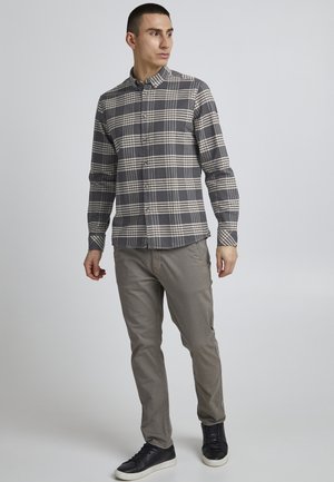 Camicia a quadri grigia e crema, maniche lunghe e colletto a punta, abbinata a pantaloni grigi chiari e sneakers nere.