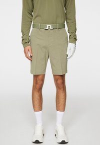 Khaki-shortsit, joissa on teksturoitu kangas, vyö hopeisella soljella, yhdistetty valkoisiin lenkkitossuihin ja sukkiin, pitkähihainen oliivinvihreä paita.