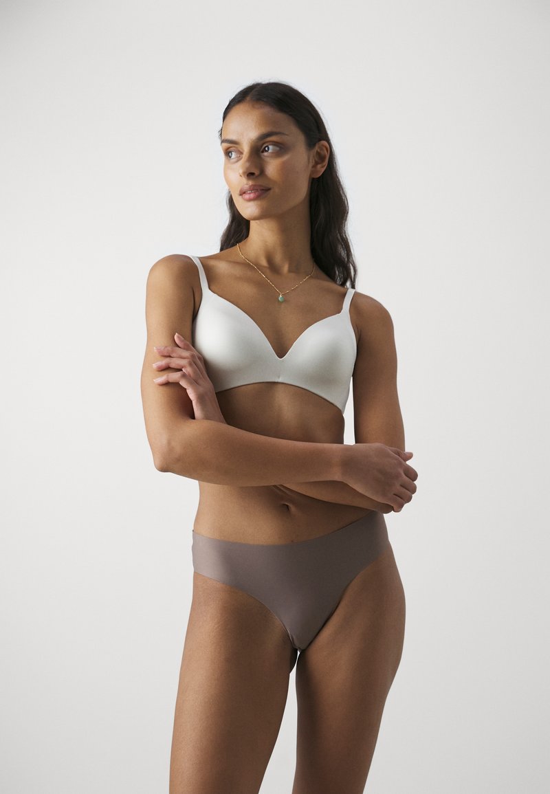 Weißer gepolsterter BH mit tiefem Ausschnitt und verstellbaren Trägern, kombiniert mit glatten braunen High-Waist-Slips. Einfaches und nahtloses Design.
