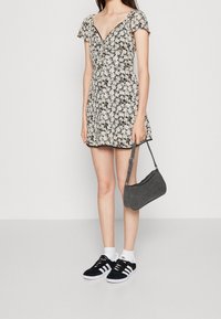 Schwarzes Blumendruckkleid mit kurzen Ärmeln, V-Ausschnitt und ausgestelltem Rock. Kombiniert mit schwarzen Turnschuhen und einer grauen Wildleder-Schultertasche.
