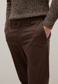 Bruine chino's gemaakt van gladde stof, met een getailleerde pasvorm, zijzakken en riemlussen. De trui heeft een gemêleerd breiknittedesign.
